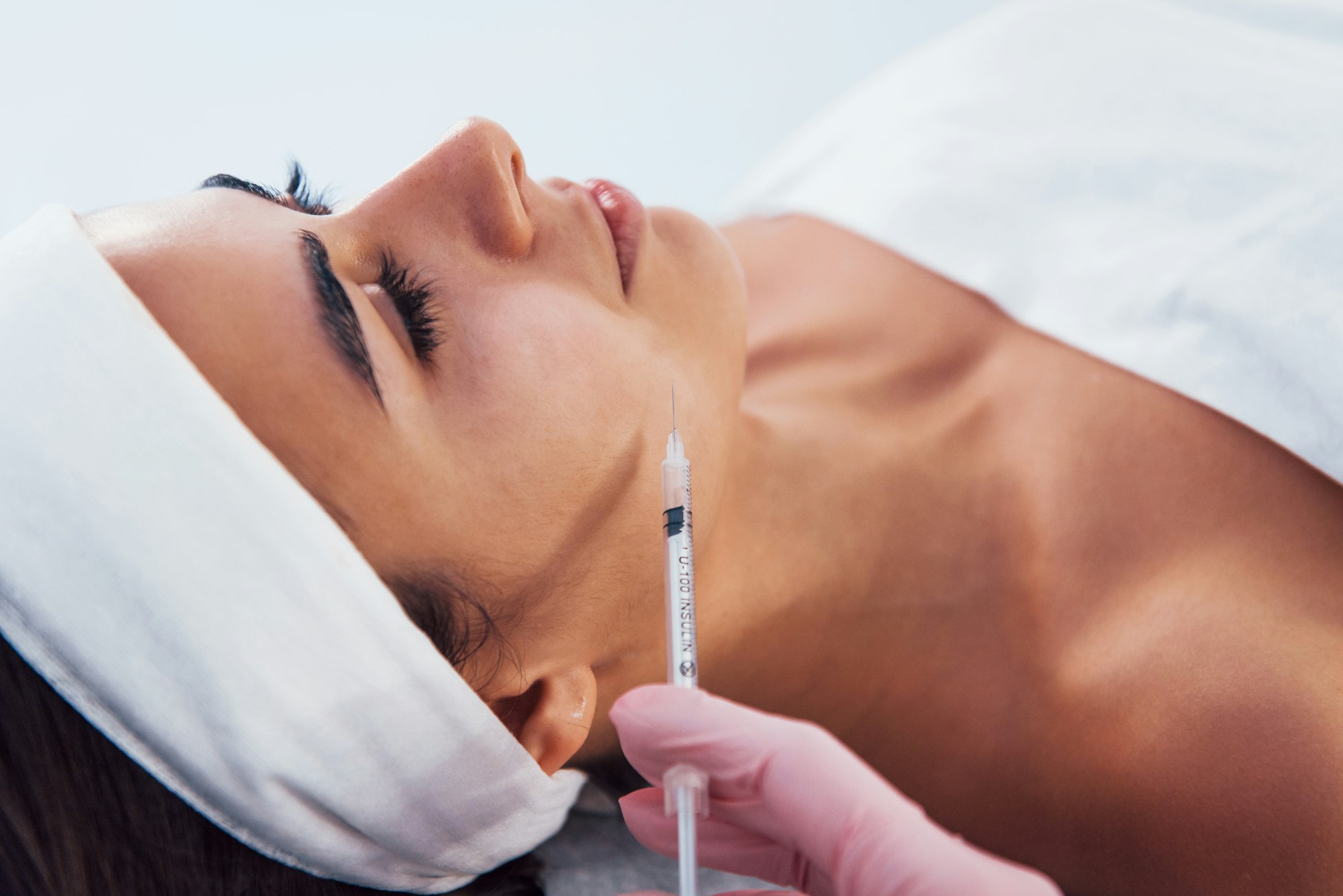 Woman that lying down in spa salon and have injection by the syringe into her face skin